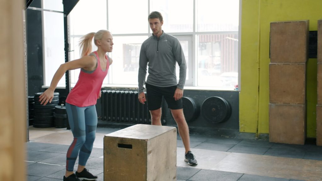 Woman jumping onto box with trainer watching
