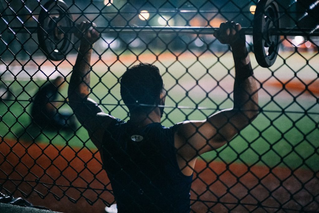 a man holding a barbell behind a fence
