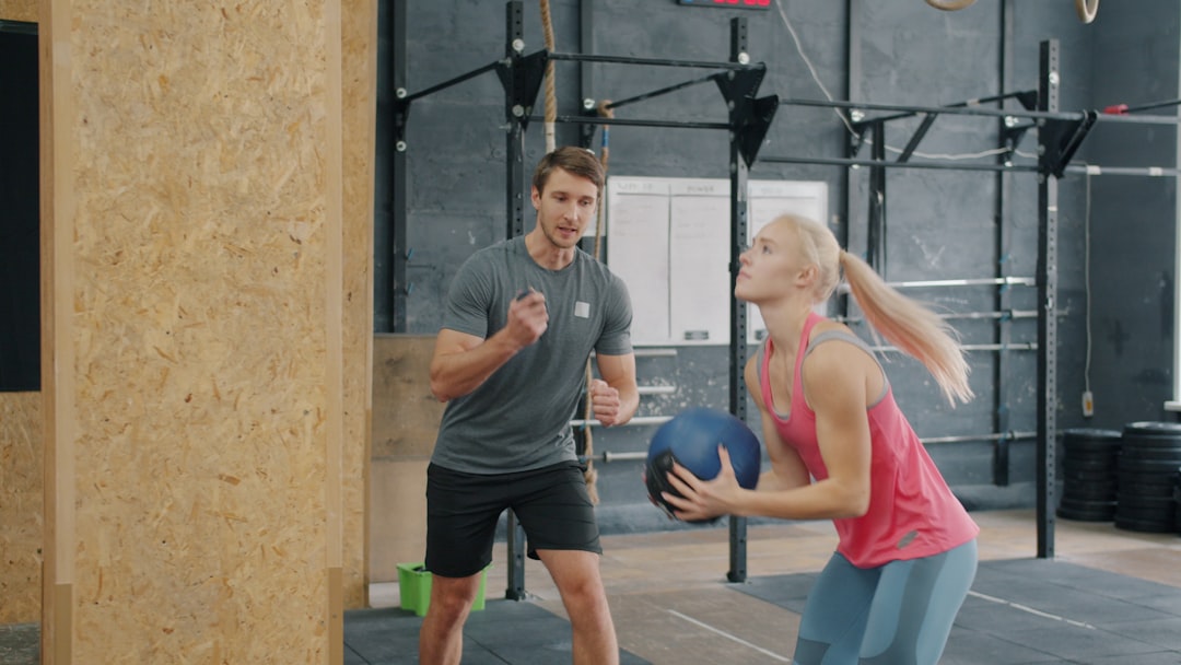 A woman holding a medicine ball with a trainer watching.