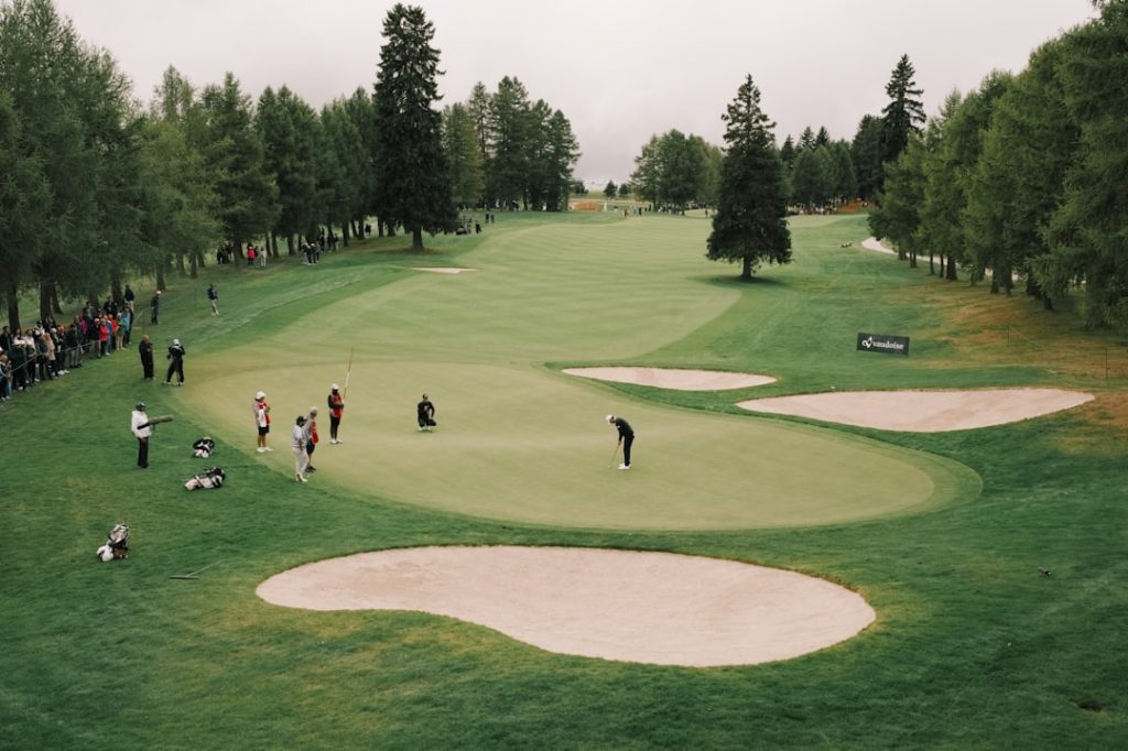 Golfers on a green with sand traps and trees.
