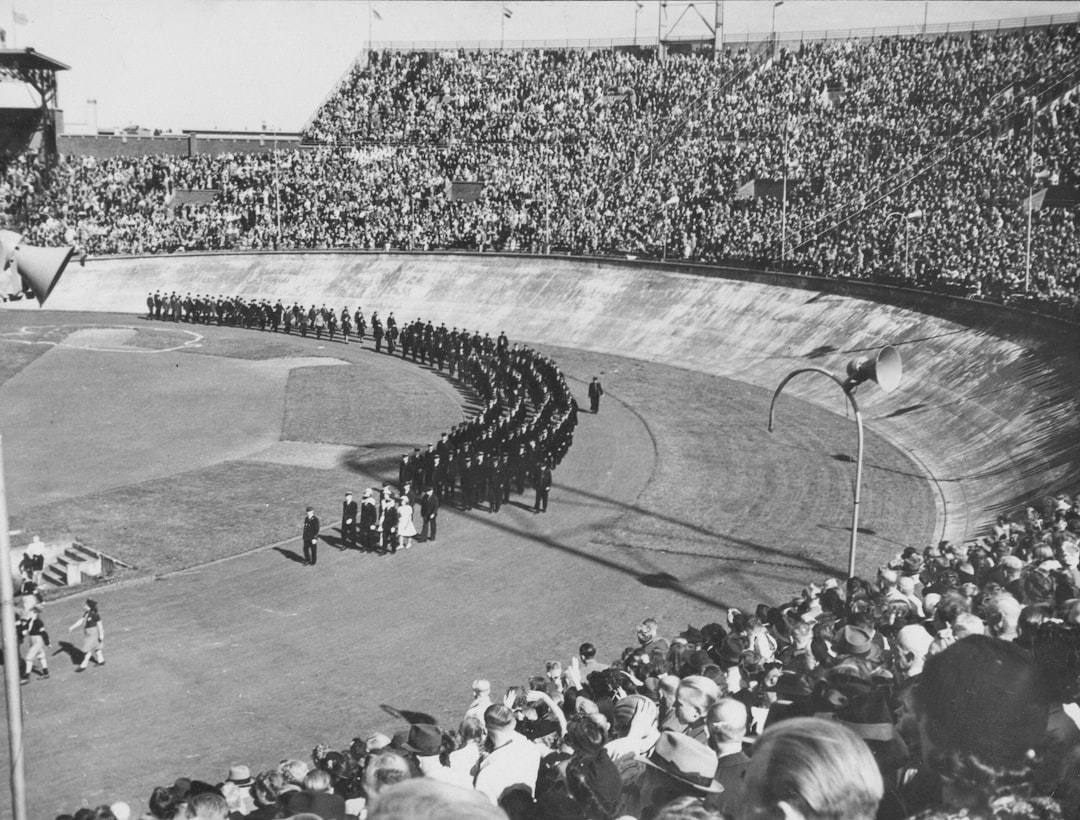 A large crowd watches a procession on a stadium track.