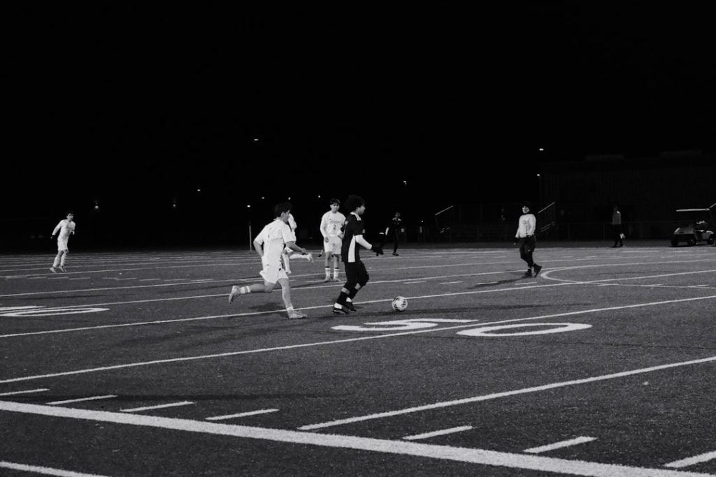 Soccer players compete on a field at night