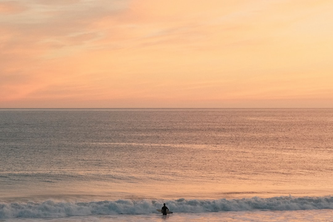 A surfer enjoys the calm ocean at sunset.