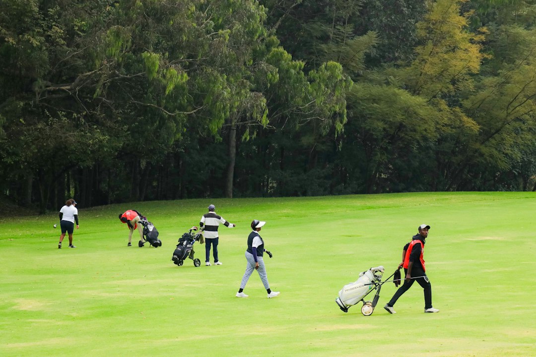 People walking across a green golf course with bags and clubs