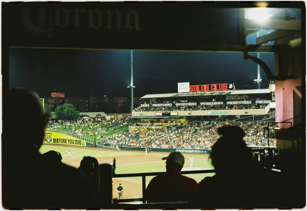 Silhouetted spectators watching a night baseball game from a stadium suite
