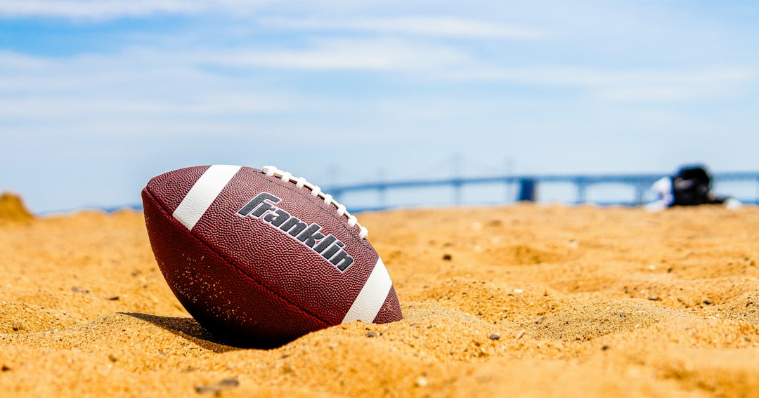 American football partially buried in sand on a sunny beach
