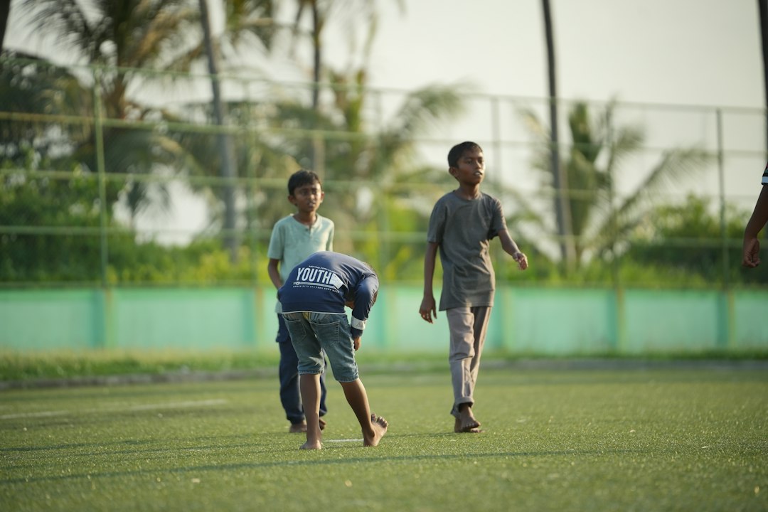 Three children on a green sports field with a fence in the background