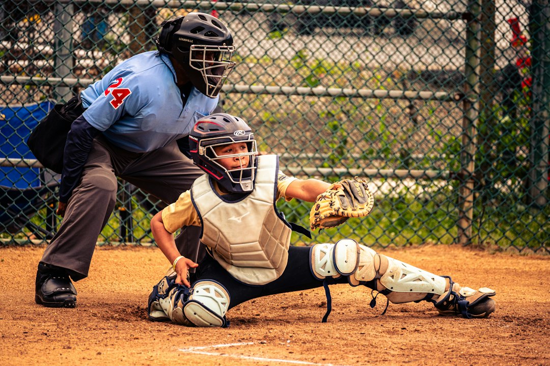 A baseball catcher in protective gear reaching for a ball behind an umpire