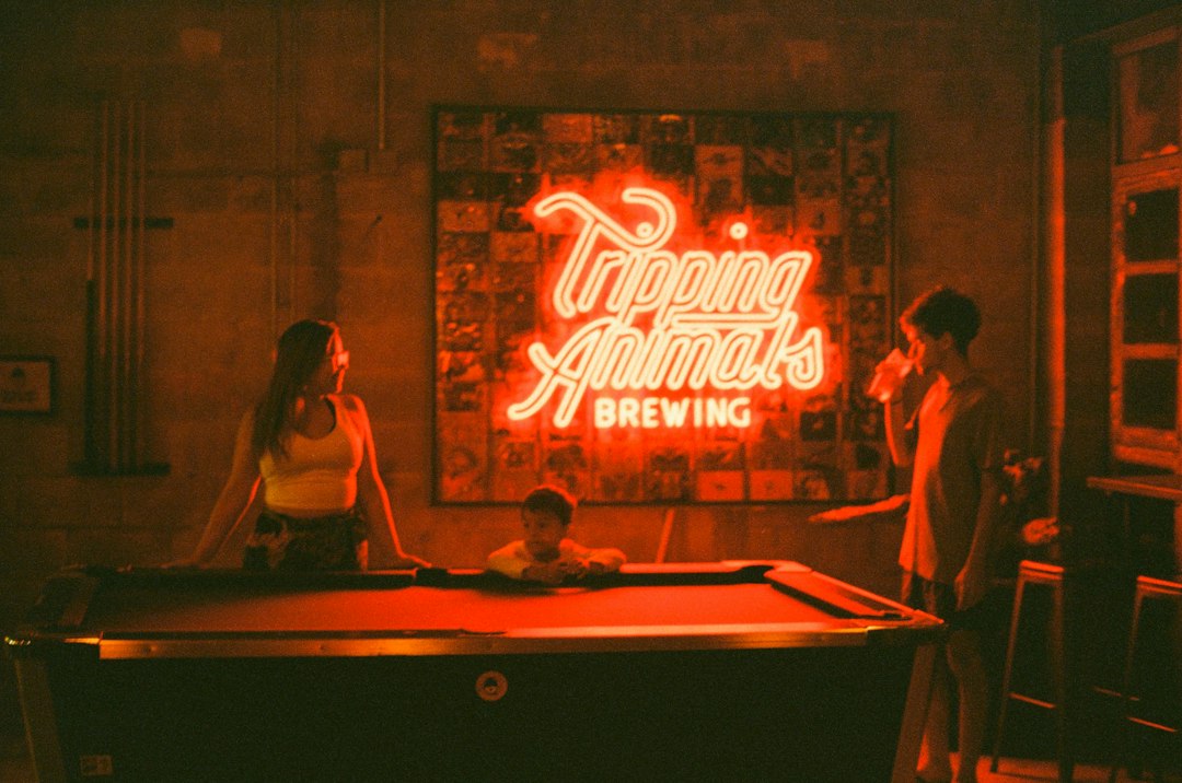 People playing pool under a "tripping animals brewing" neon sign
