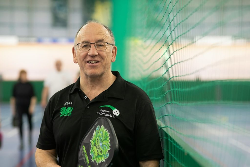 A smiling man holds a pickleball paddle