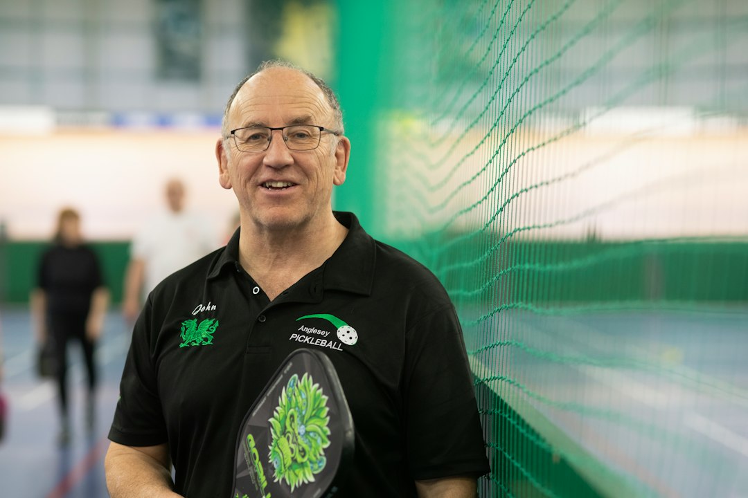 A smiling man holds a pickleball paddle