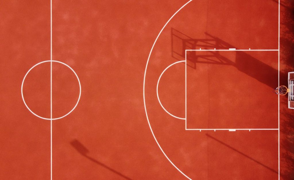 An aerial view of a red basketball court with white lines and shadows