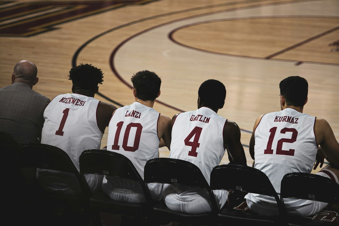 four basketball players sitting near another man in basketball court